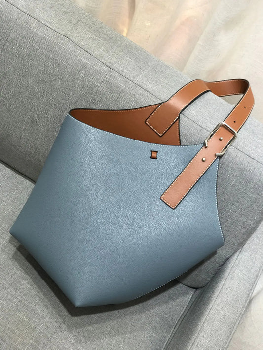 Blue handbag with brown leather strap on a gray surface