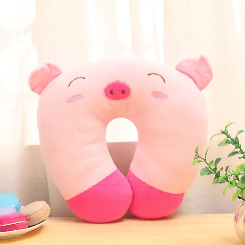 Pink pig-shaped neck pillow on a light surface with a plant in the background