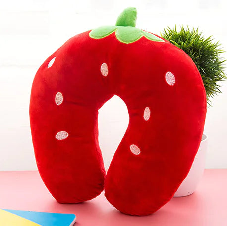 Red strawberry-shaped neck pillow on a pink surface with a white background